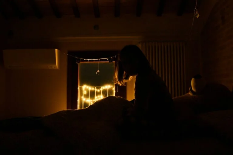 A person sitting up in bed in a dark bedroom at night, awake and unable to get back to sleep