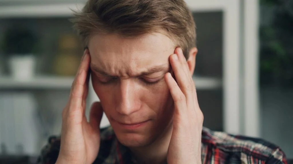 A man with his eyes closed pressing his fingertips to his temples during a headache