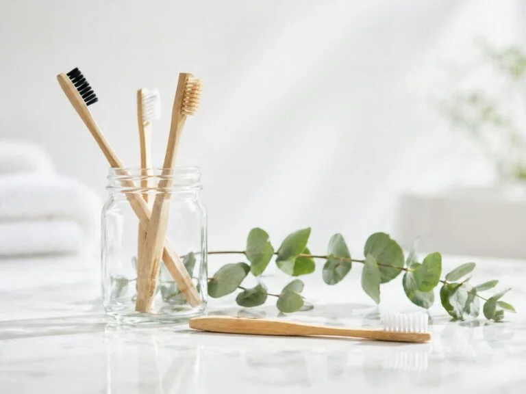 Bamboo toothbrushes in a glass jar beside a sprig of eucalyptus