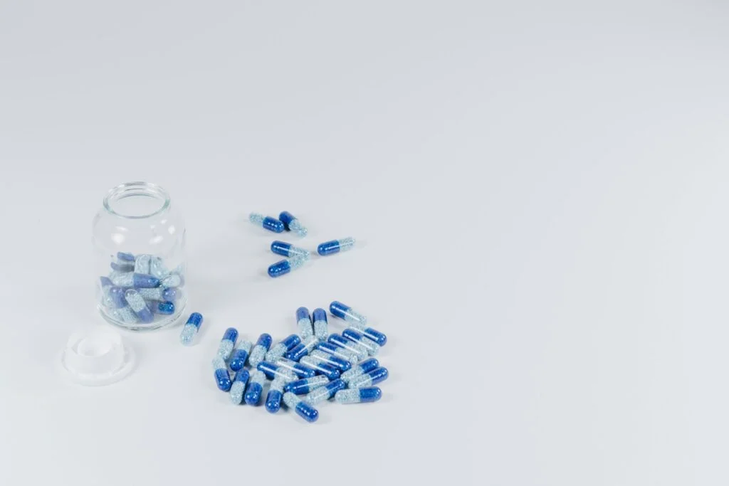 Blue capsules spilling from a small glass jar on a white table