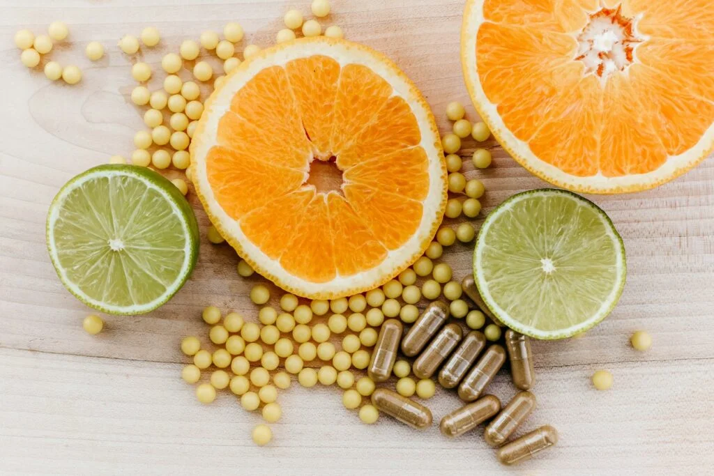 Capsules and softgels beside sliced oranges and limes on a wooden board
