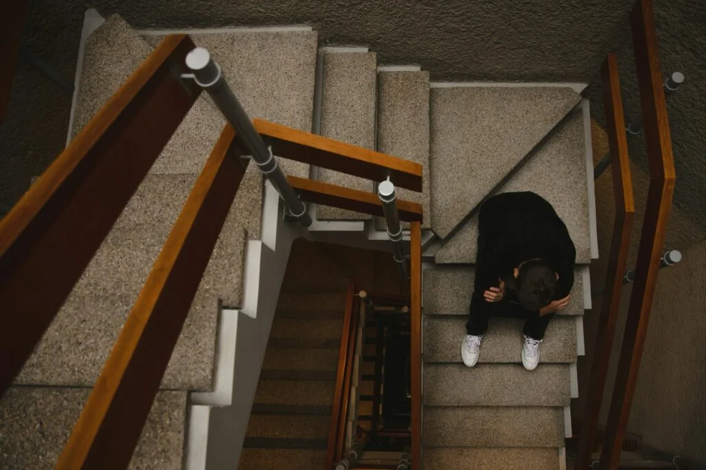 A person sitting alone on a stairwell with their head in their hands