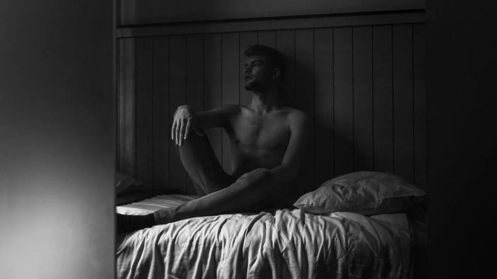 Man sitting up awake in bed in a dark room