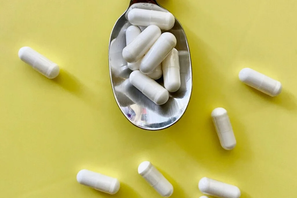 White capsules in a metal spoon on a yellow background