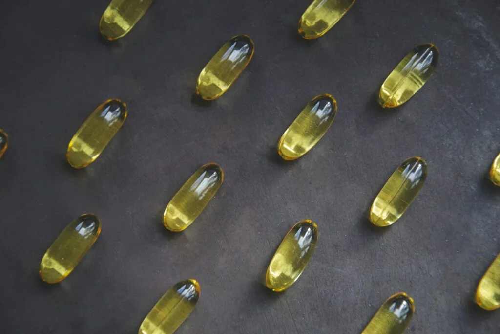 Golden omega 3 softgel capsules laid out on a dark surface