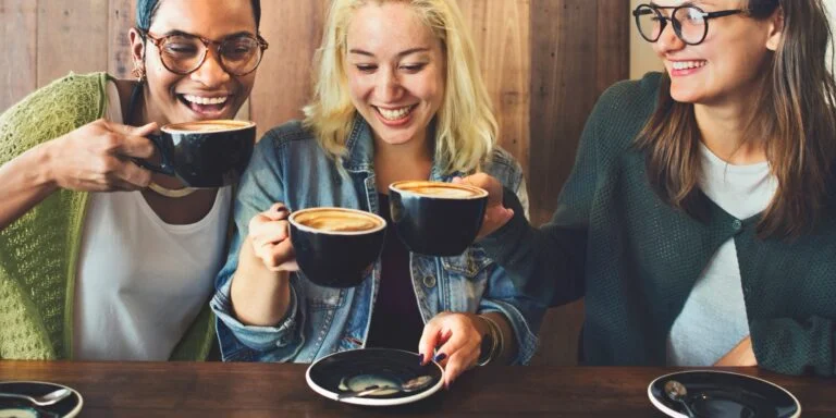 Three friends laughing together over coffee