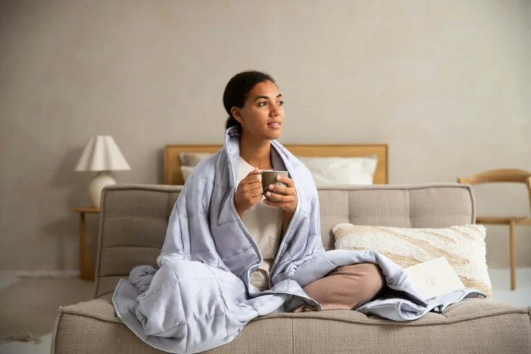 A woman wrapped in a soft blanket on a sofa holding a warm drink