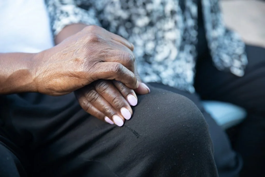 An older person's hands resting together on their knee