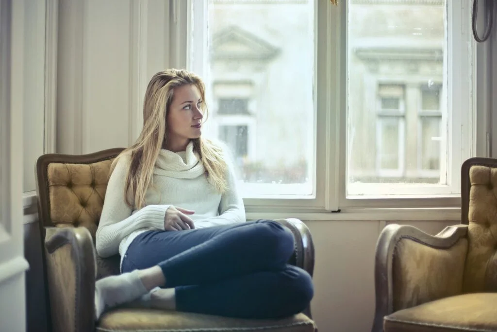 Woman sitting in an armchair by a window, looking thoughtful