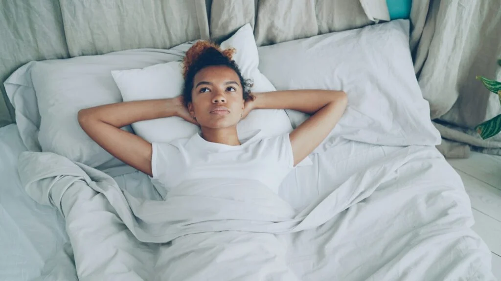 Woman lying on her back in bed with hands behind her head, relaxing