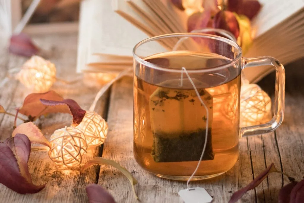 Glass mug of herbal night time tea with candles and autumn leaves