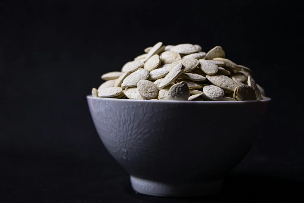 A bowl of pumpkin seeds against a dark background