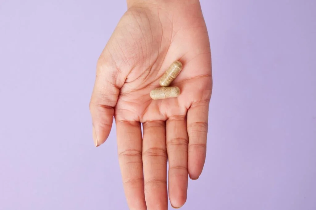 Two capsules held in an open hand on a lilac background