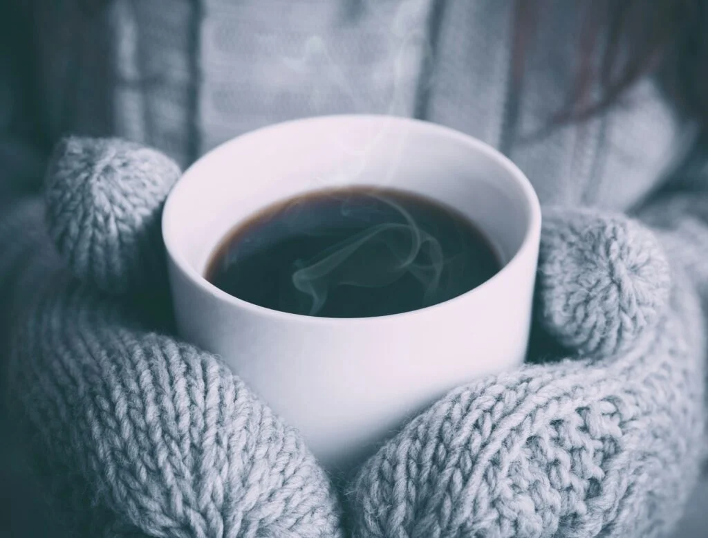 Hands in grey knitted mittens holding a hot drink