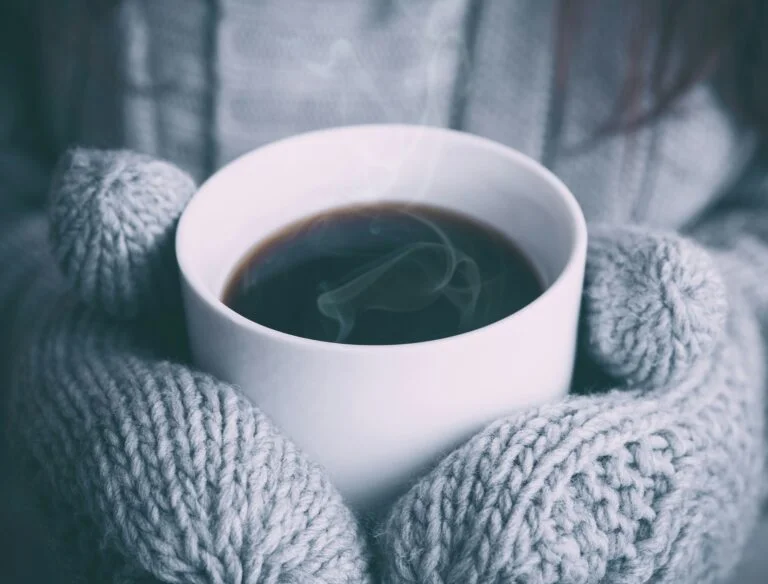 Hands in grey knitted mittens holding a hot drink