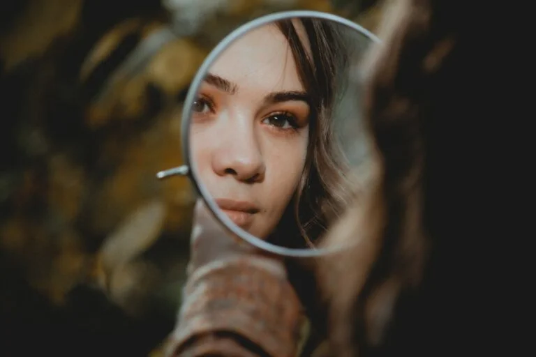 Woman checking her face in a small round mirror, looking at redness on her cheeks