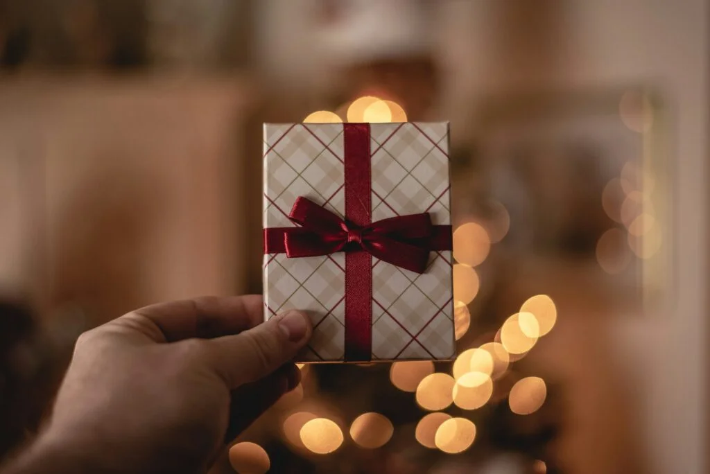 A hand holding a small wrapped gift in front of Christmas lights