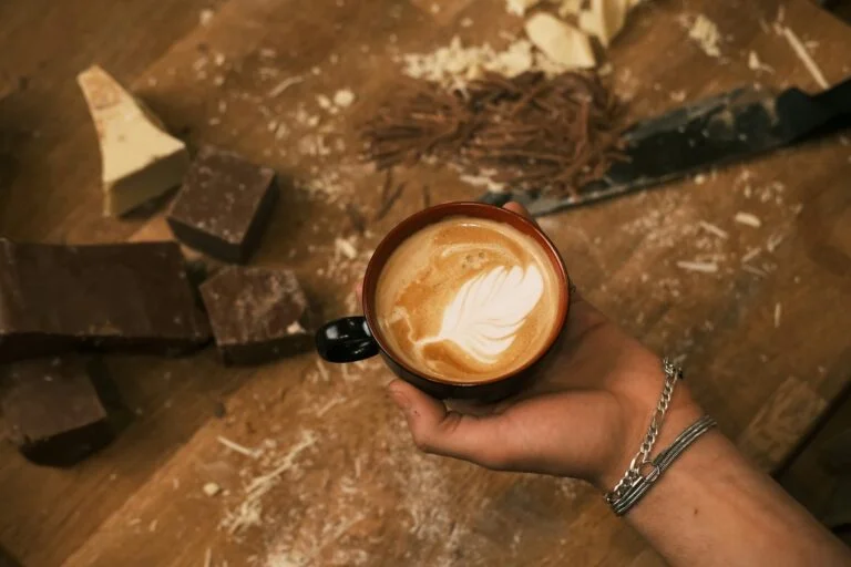 A hand holding a cup of coffee over a wooden table
