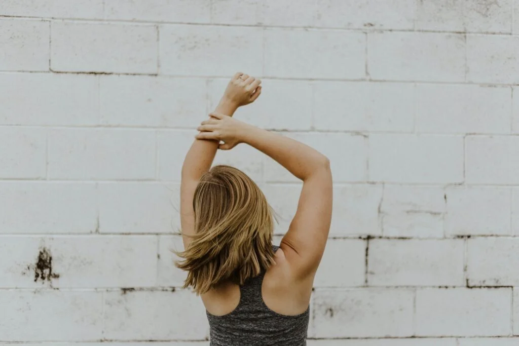 Woman stretching her arms and shoulders overhead against a white wall