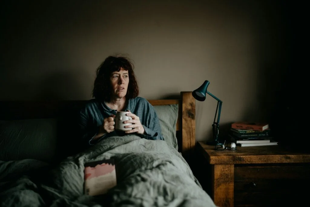 Woman sitting awake in bed at night holding a mug