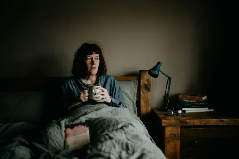 Woman sitting awake in bed at night holding a mug
