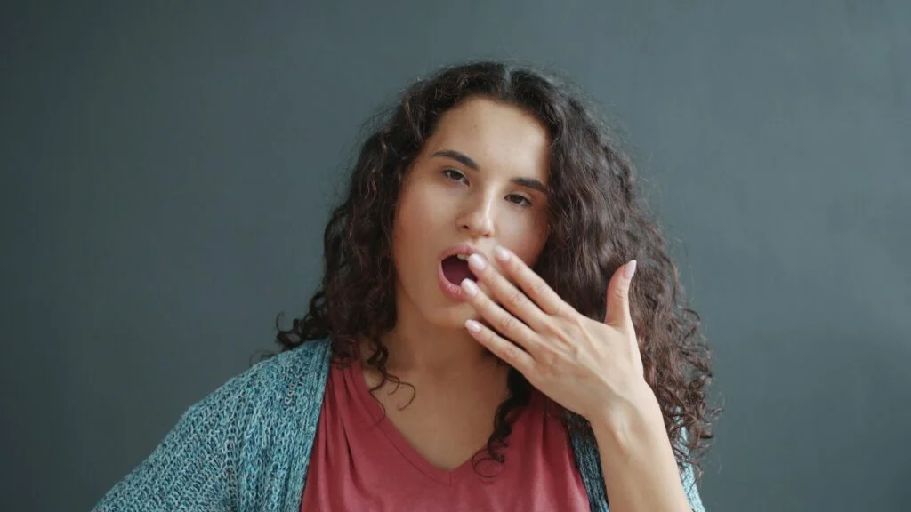 Young woman yawning with her hand over her mouth