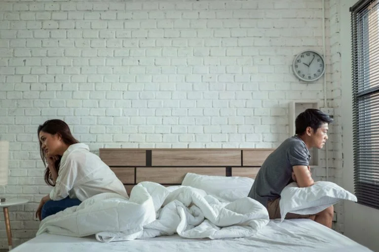 A couple sitting in bed, not talking to each other