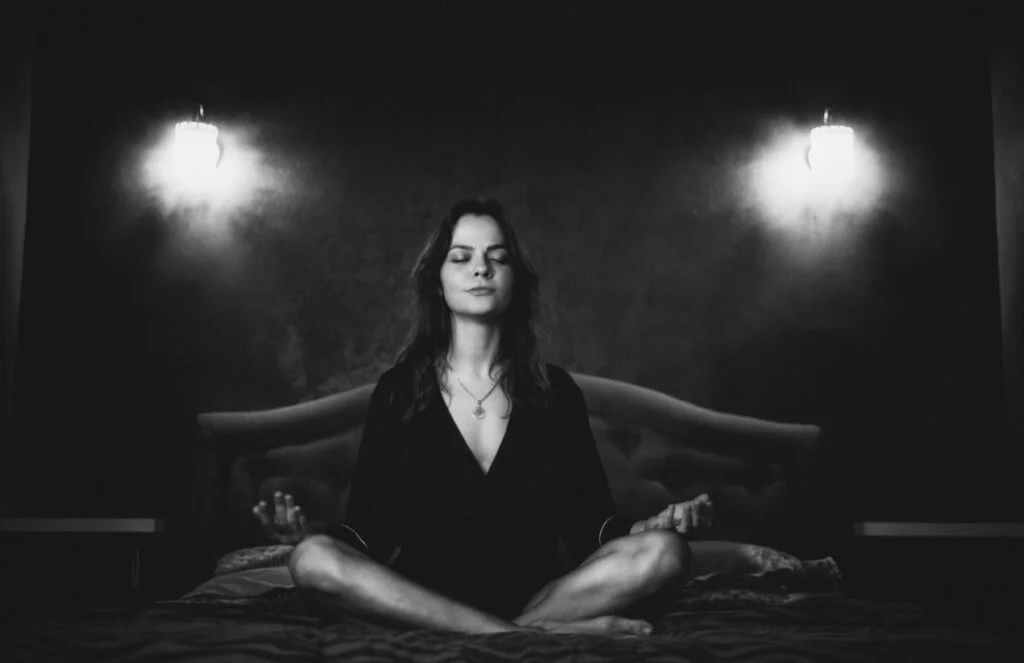 Woman meditating cross-legged on her bed at night