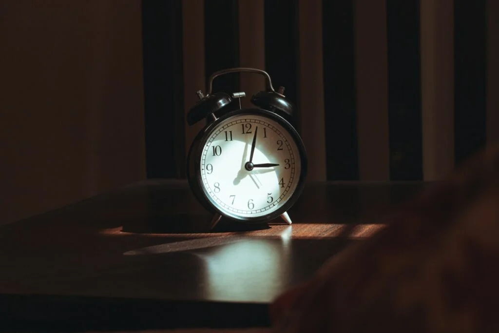 A classic alarm clock on a bedside table in a dark room