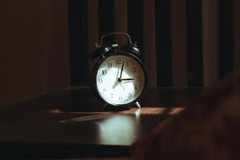 A classic alarm clock on a bedside table in a dark room