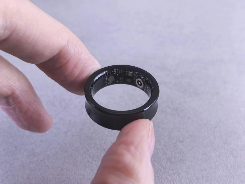 Fingers holding a smart sleep tracking ring showing its sensors