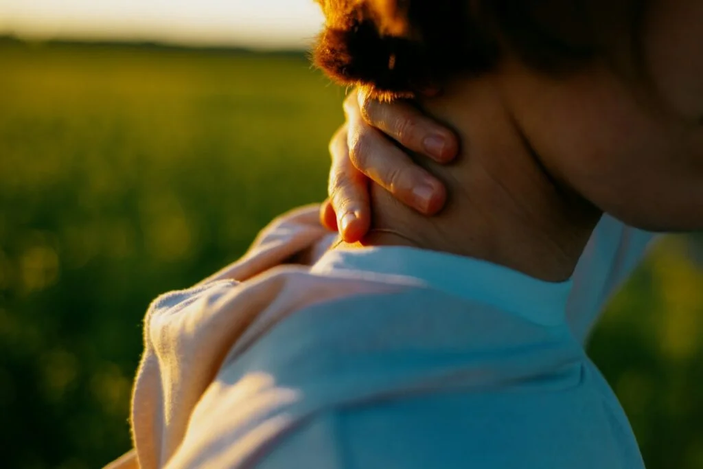 A person holding the back of their neck in evening sunlight