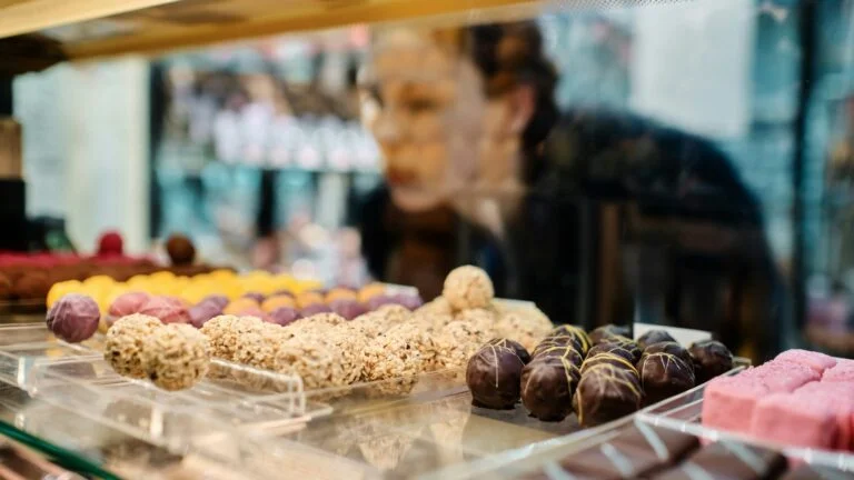 A woman looking through a glass counter at chocolate truffles and sweets