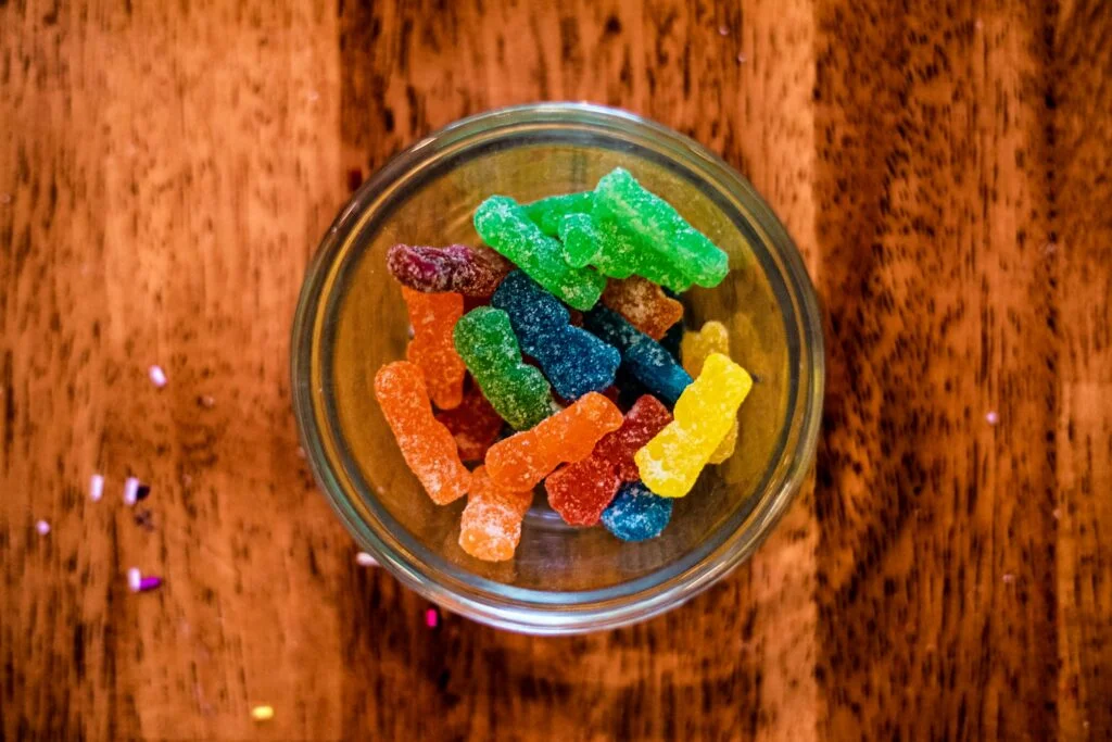A small glass bowl of colourful sugar-coated gummy bears on a wooden table