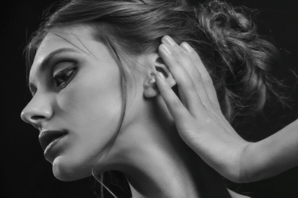 A woman cupping her hand behind her ear, black and white portrait