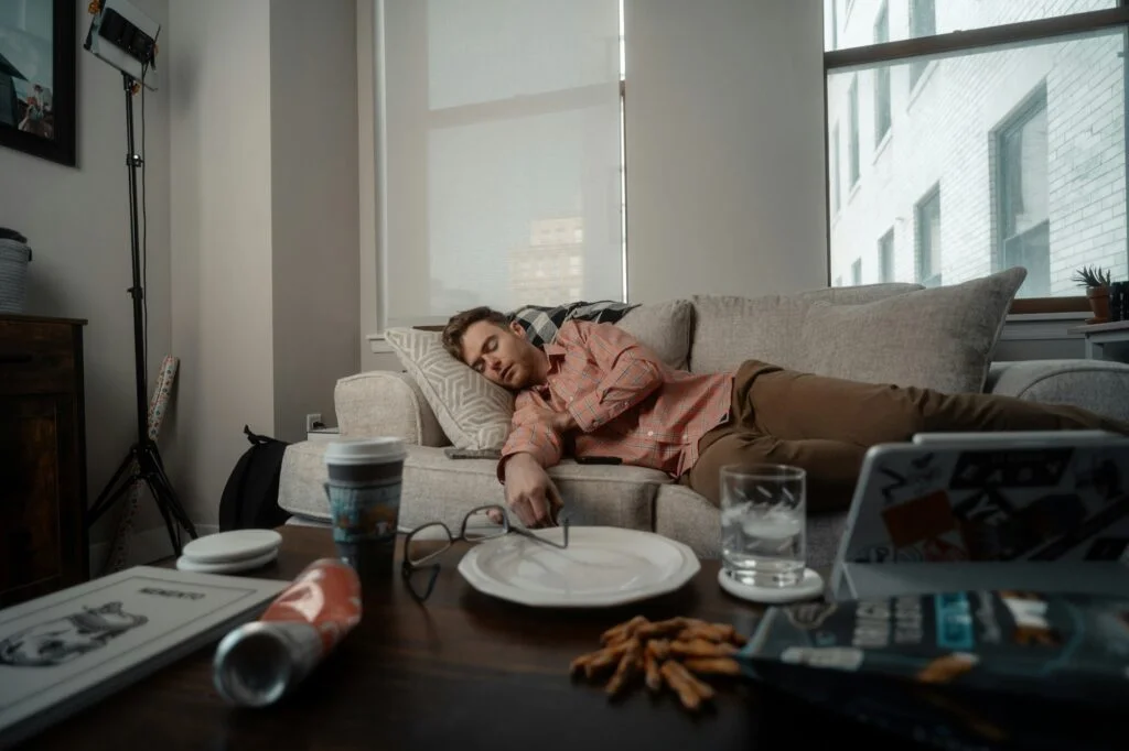 Man asleep on a sofa next to an empty plate after a meal