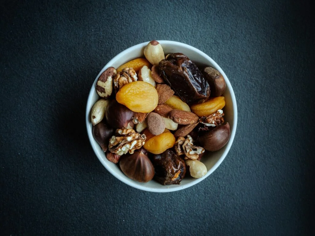 A bowl of mixed nuts and dried fruit on a dark surface