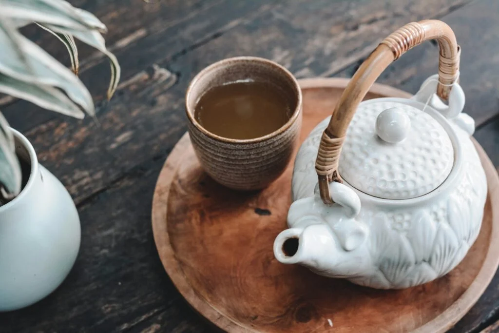 A white teapot and a cup of herbal tea on a wooden tray