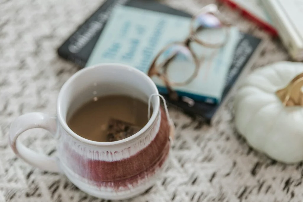 A mug of herbal tea with a tea bag beside a book