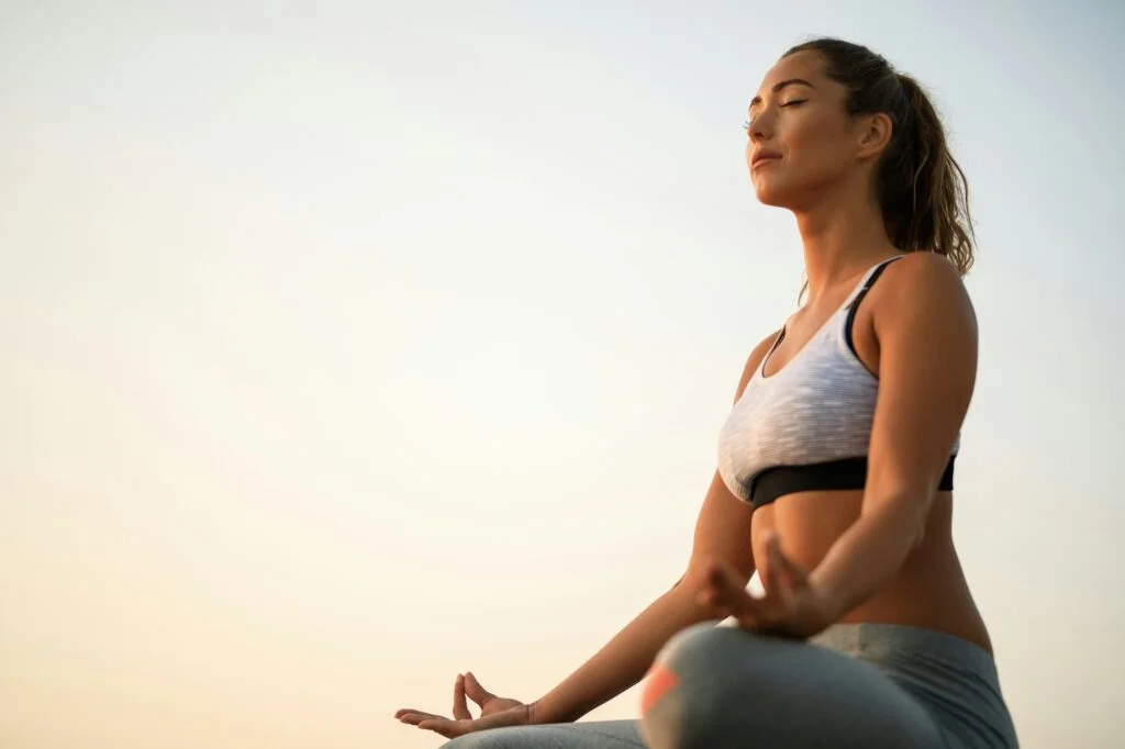 Woman breathing slowly with eyes closed, sitting cross-legged in soft evening light
