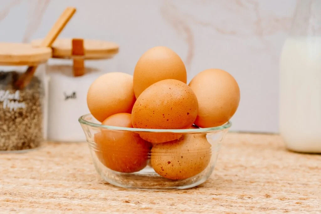 A glass bowl of brown eggs on a kitchen counter beside a bottle of milk