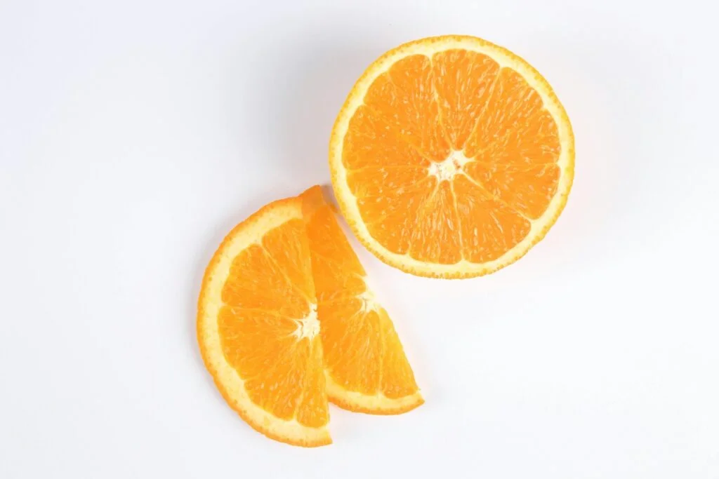 A halved orange and two orange slices on a white surface