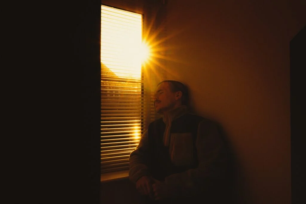 Man with eyes closed catching low winter sunlight through a window