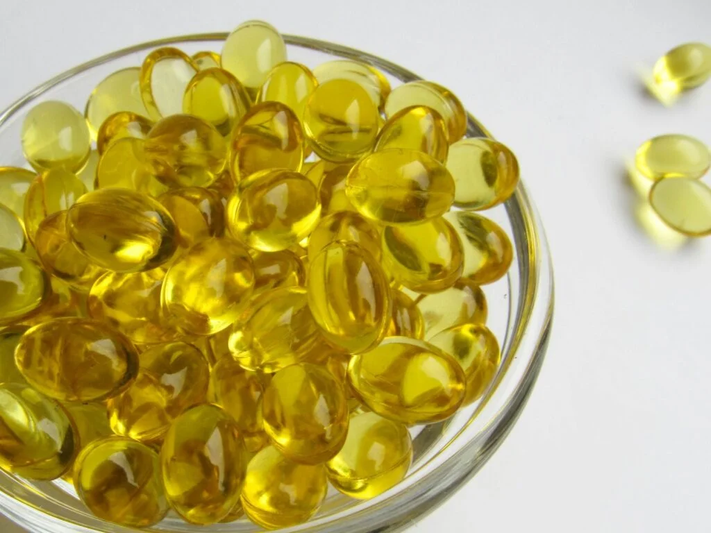 Bowl of golden vitamin D softgel capsules on a white table
