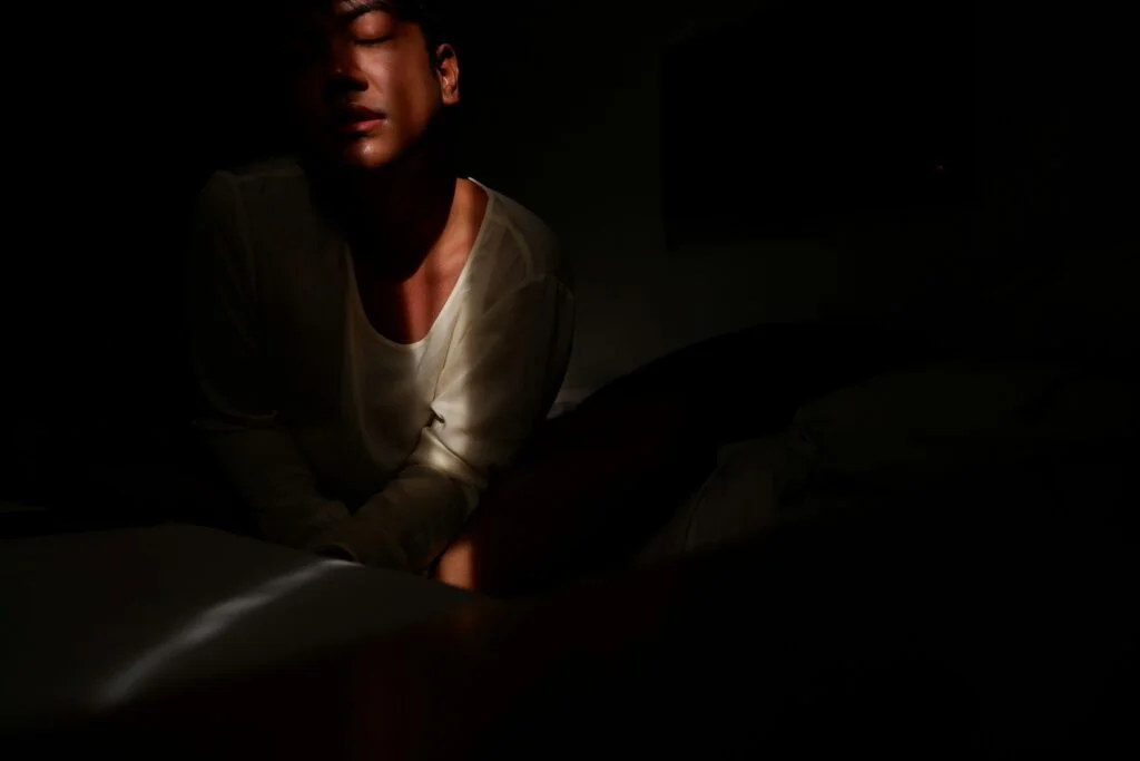 A man sitting up in bed in a dark room at night