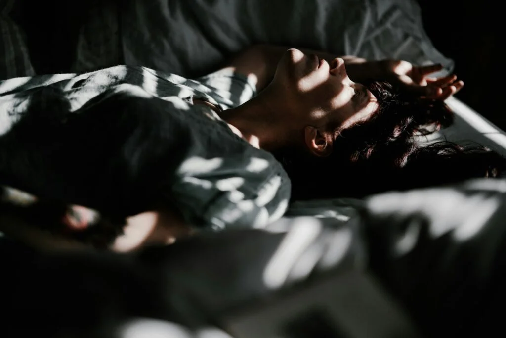 A person lying awake in bed in a dark room, arm over their face