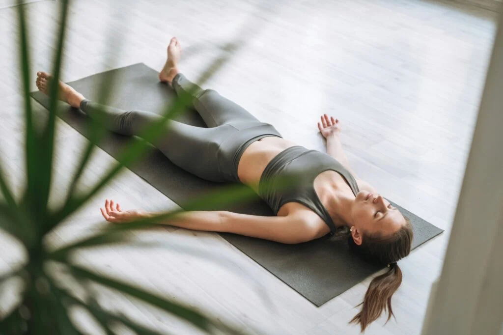 A woman lying on a yoga mat in a calm room doing yoga nidra