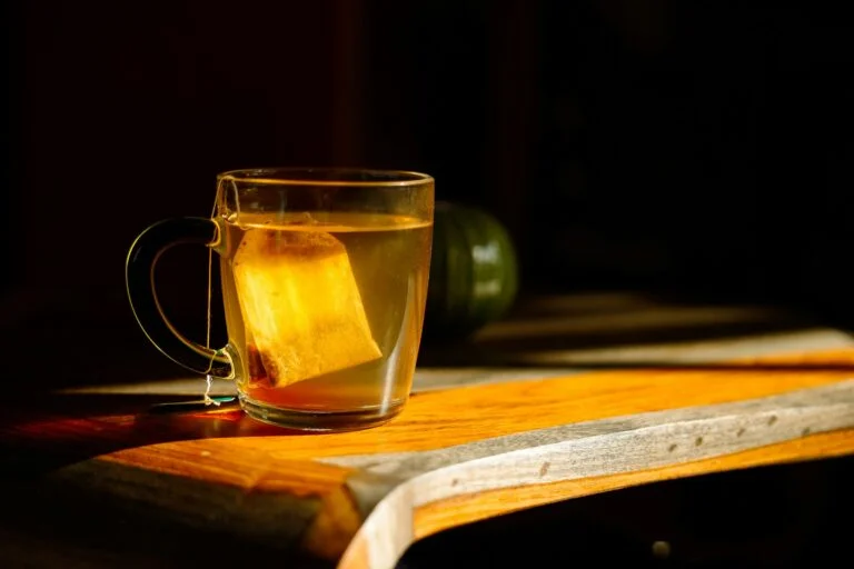 A glass mug of herbal tea with the tea bag in, lit by evening light