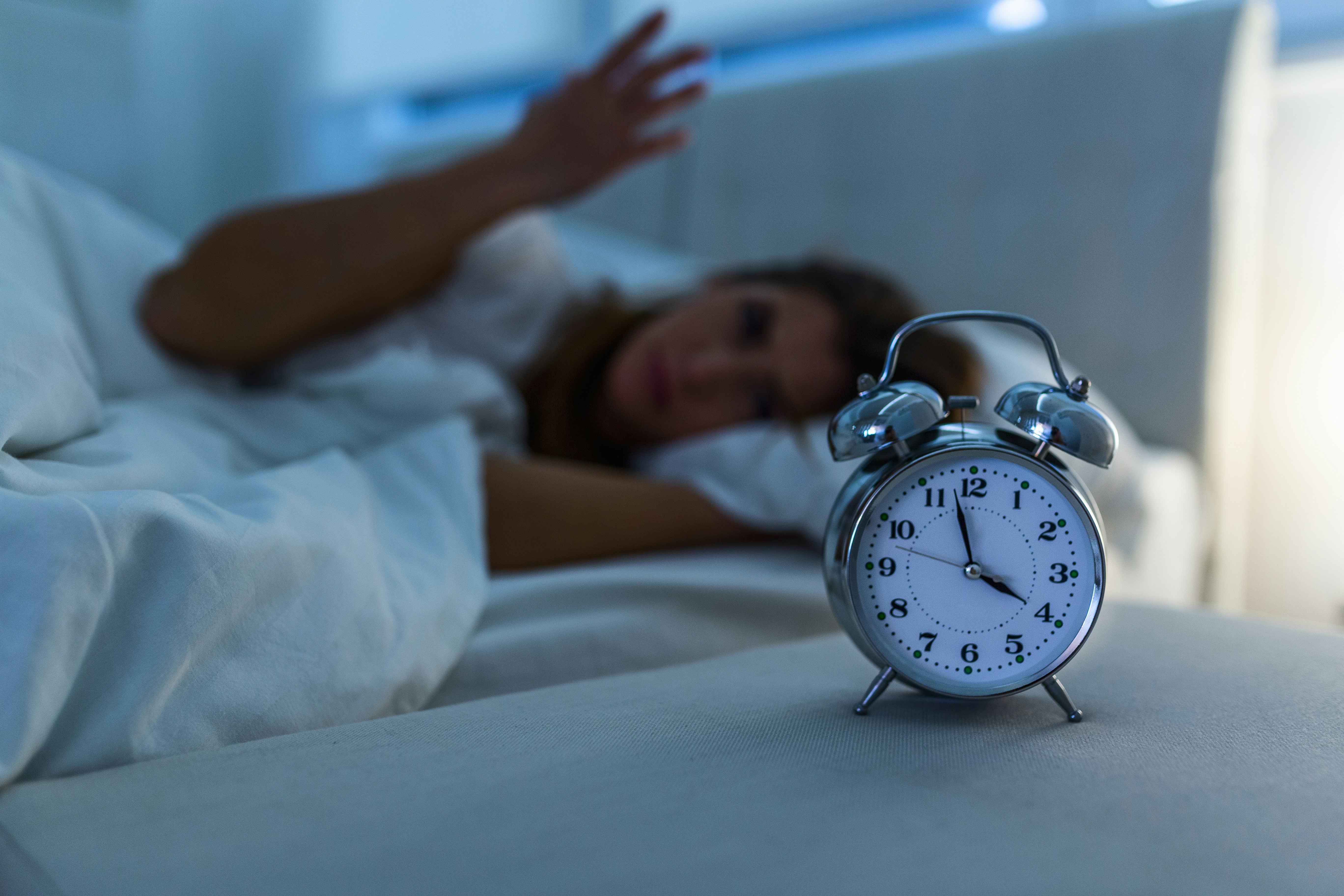 A person reaching for an alarm clock on bedside table at night