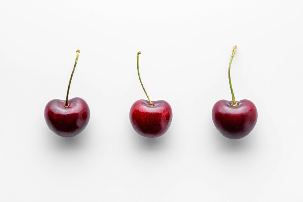 three cherries on a row on a white surface